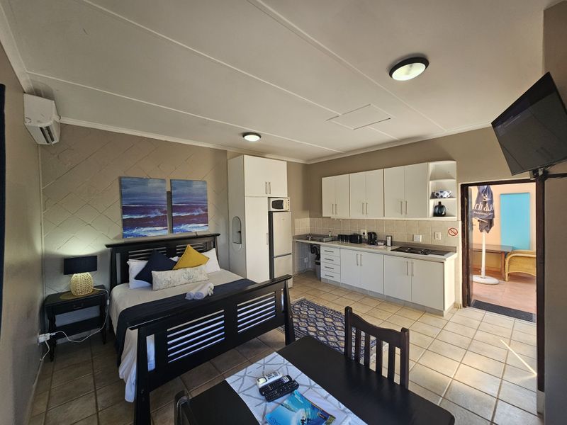An open-plan studio apartment featuring a combined bedroom and kitchenette area with tiled floors, built-in cabinetry, and direct access to an outdoor patio.