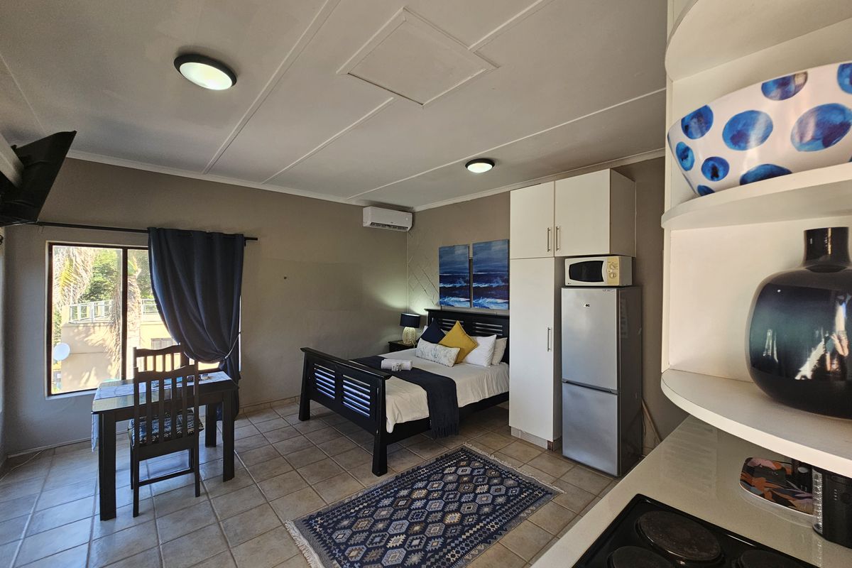 Open-plan studio apartment featuring tiled flooring, built-in cabinetry, an electric hob, and an integrated air conditioning unit.