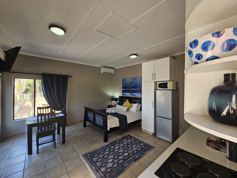 Open-plan studio apartment featuring tiled flooring, built-in cabinetry, an electric hob, and an integrated air conditioning unit.