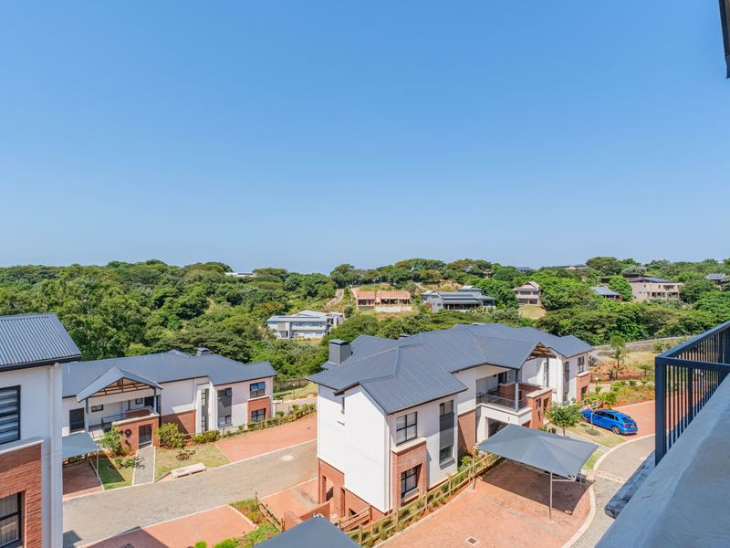 Elevated view overlooking a modern residential apartment complex with paved driveways, carports, and surrounding lush green landscape.