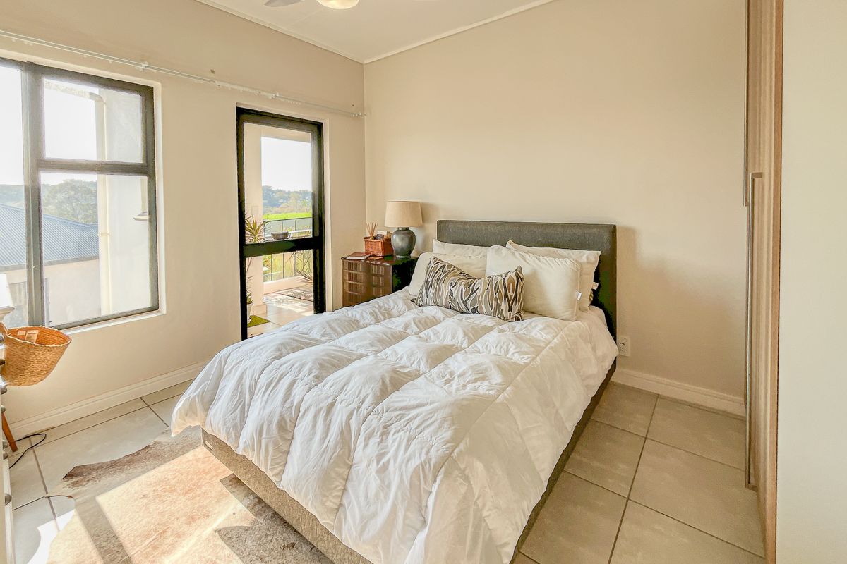 A well-lit bedroom featuring tiled flooring, a built-in wardrobe, a ceiling fan, and direct access to a private balcony through a sliding glass door.