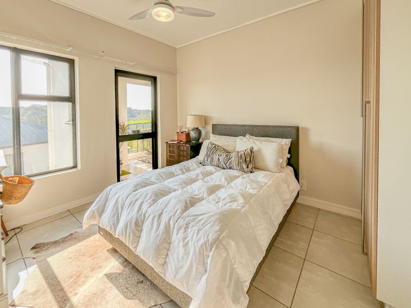A well-lit bedroom featuring tiled flooring, a built-in wardrobe, a ceiling fan, and direct access to a private balcony through a sliding glass door.