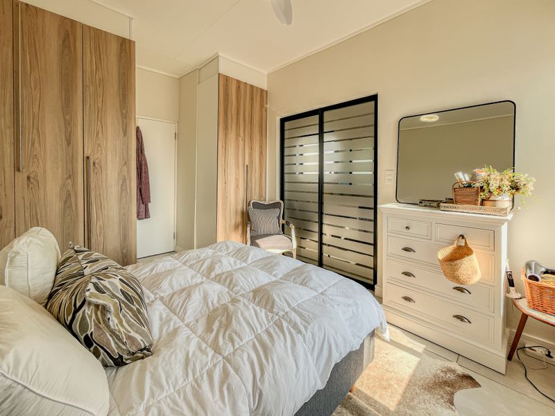 A well-maintained bedroom featuring modern wood-finish built-in cupboards, tiled flooring, and a contemporary sliding door with frosted glass detailing.