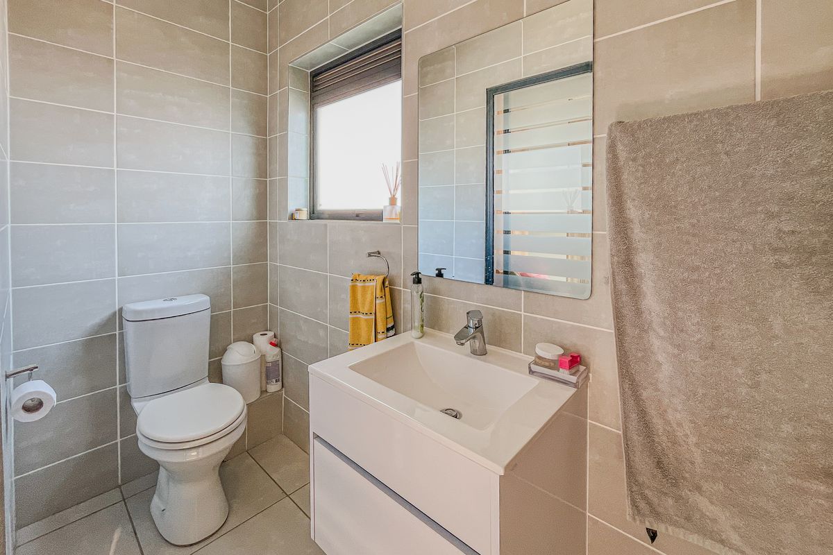 A modern, well-maintained bathroom featuring neutral wall and floor tiles, a contemporary vanity with basin, and a wall-mounted mirror.