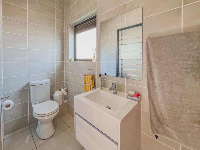 A modern, well-maintained bathroom featuring neutral wall and floor tiles, a contemporary vanity with basin, and a wall-mounted mirror.