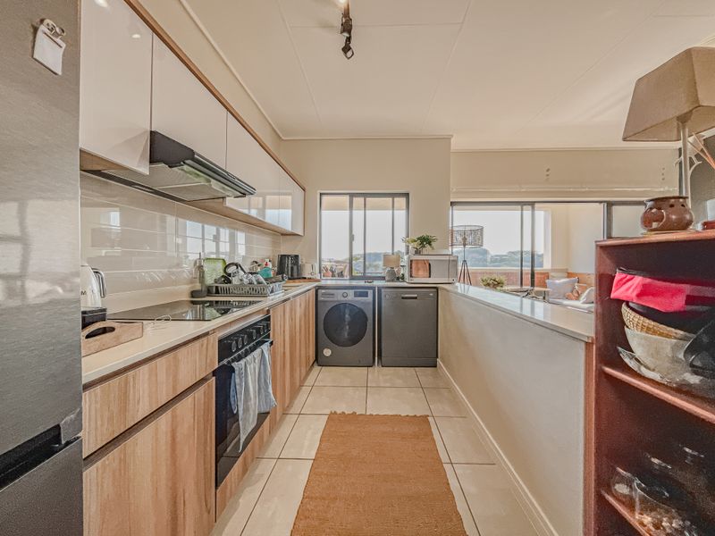 Modern kitchen featuring wood-finish cabinetry, sleek countertops, integrated appliances, and a tiled backsplash, opening into a bright living area.