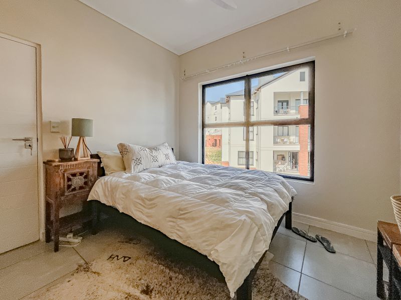 A well-lit bedroom featuring tiled flooring and a large window with views of the surrounding apartment complex.