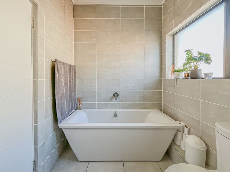 Modern bathroom featuring a sleek freestanding bathtub, wall-mounted faucet, and neutral large-format ceramic tiling throughout.