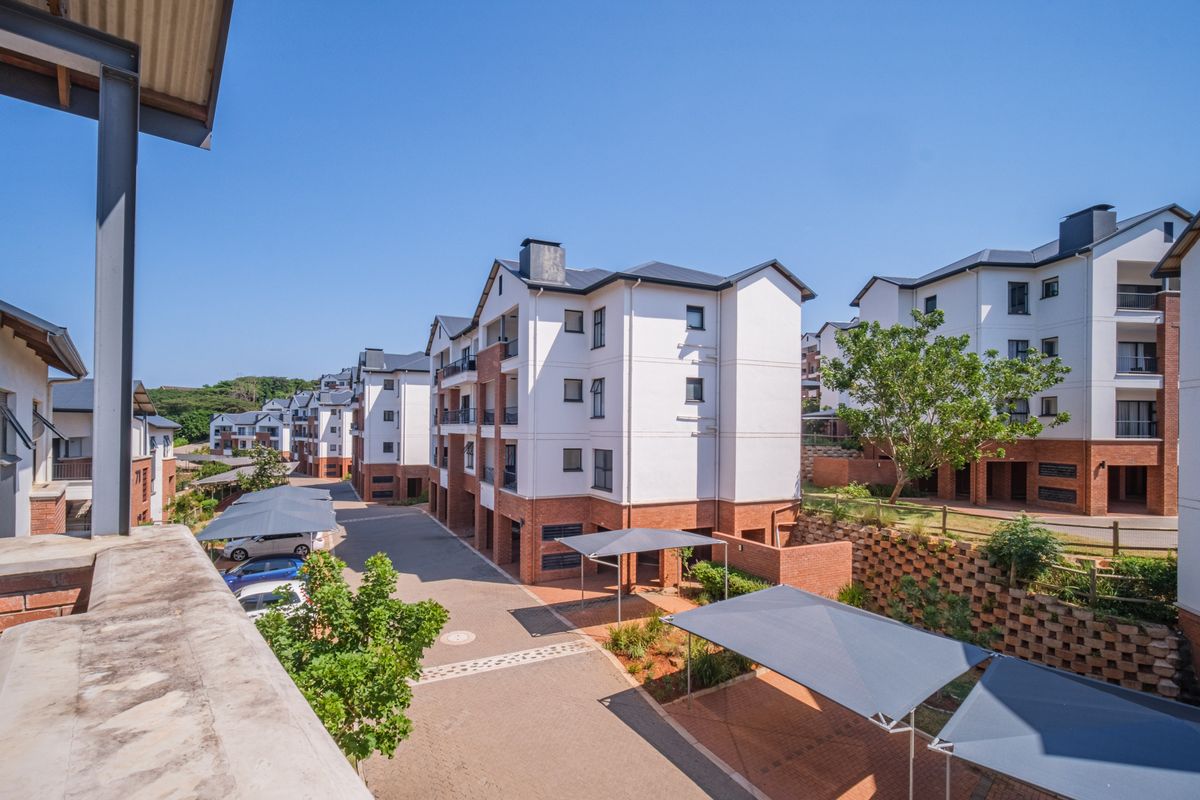 An elevated view of the apartment complex grounds, featuring paved driveways, covered parking bays, and well-maintained brick and plaster building exteriors.