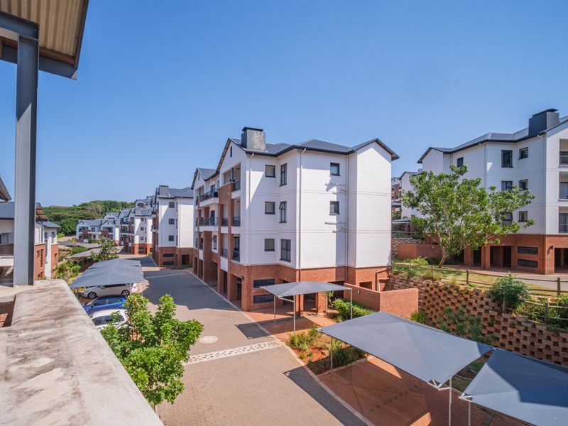 An elevated view of the apartment complex grounds, featuring paved driveways, covered parking bays, and well-maintained brick and plaster building exteriors.
