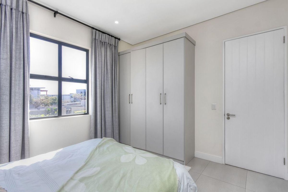 A bright bedroom featuring neutral tiled flooring, built-in grey cabinetry, and large windows with modern curtains.