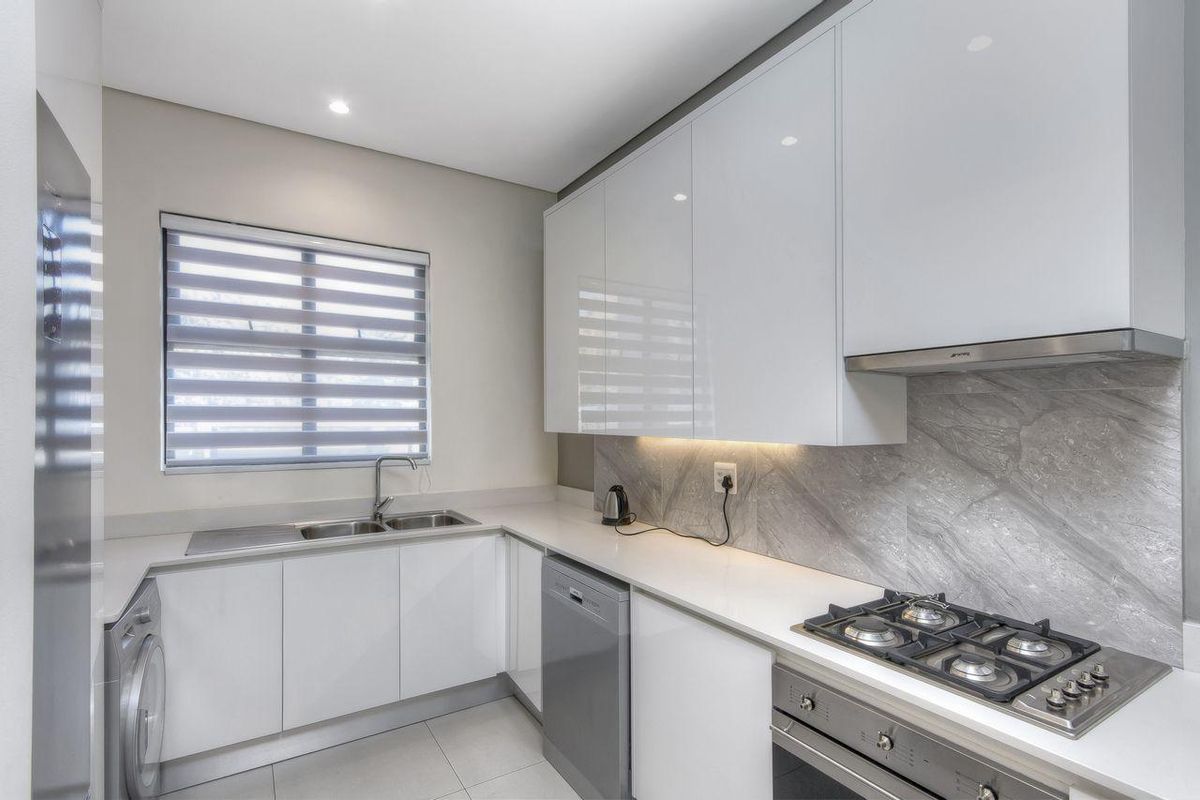 Modern kitchen featuring high-gloss white cabinetry, stone countertops, a gas hob, built-in oven, extractor fan, and integrated sink with tiled backsplash.