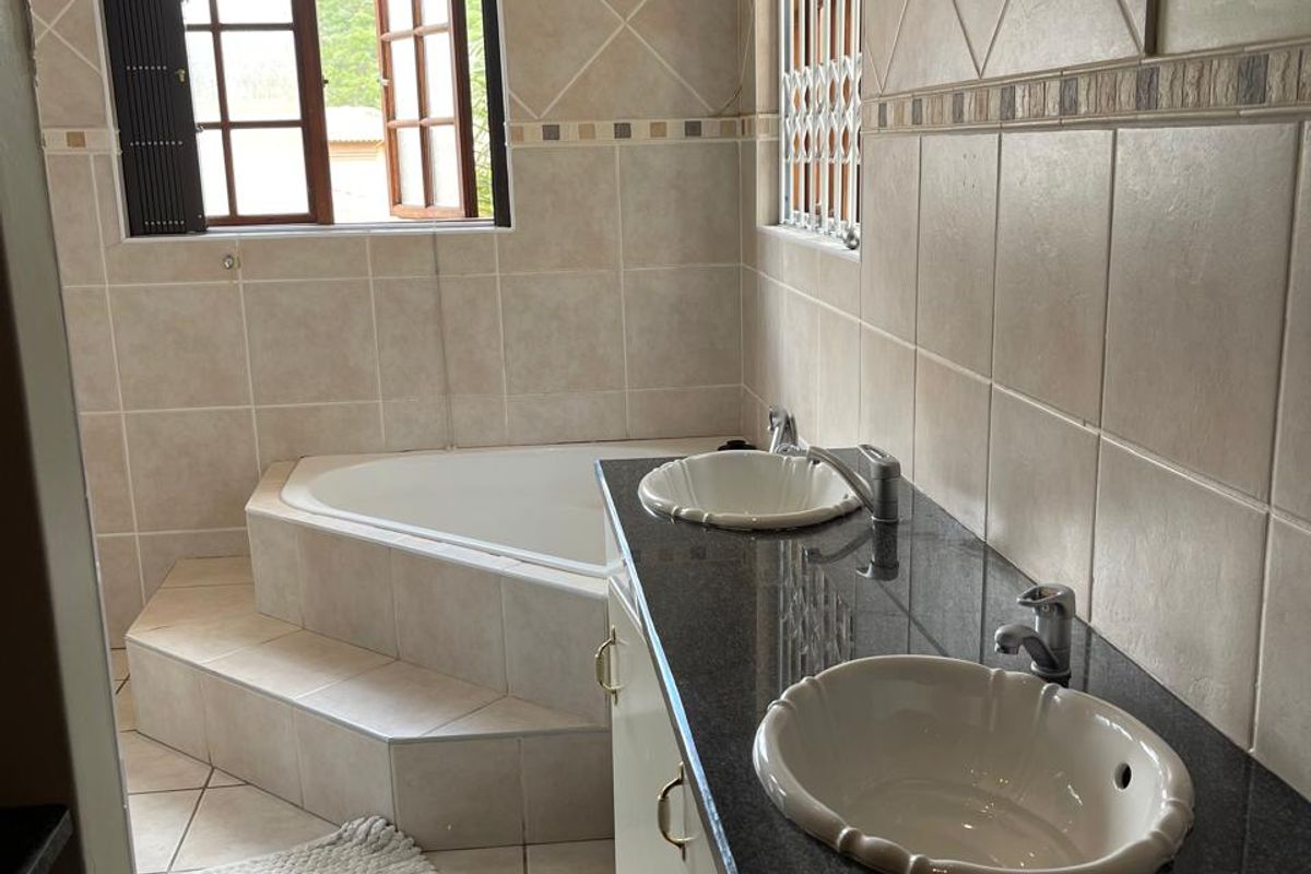 A bathroom featuring a corner bathtub, a double vanity with granite countertops, and tiled walls and flooring.