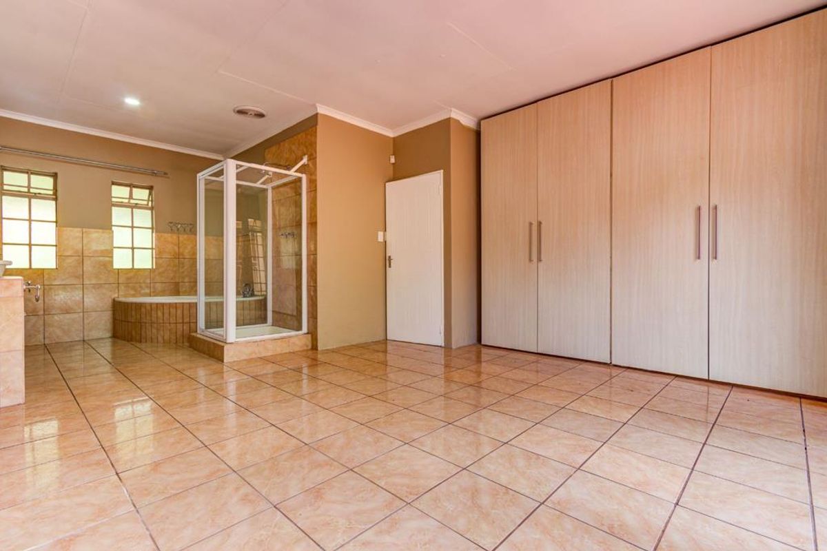 Spacious bedroom featuring extensive built-in cupboards, tiled flooring, and an open-plan en-suite bathroom with a corner bathtub and separate shower cubicle.
