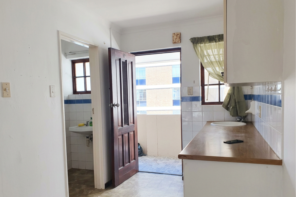 A compact kitchen area featuring a wooden countertop, tiled splashback, and direct access to an external balcony, with an adjacent bathroom visible.