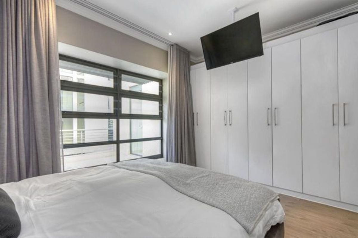 A well-maintained bedroom featuring extensive floor-to-ceiling built-in cabinetry, modern horizontal pane windows, and elegant crown molding.