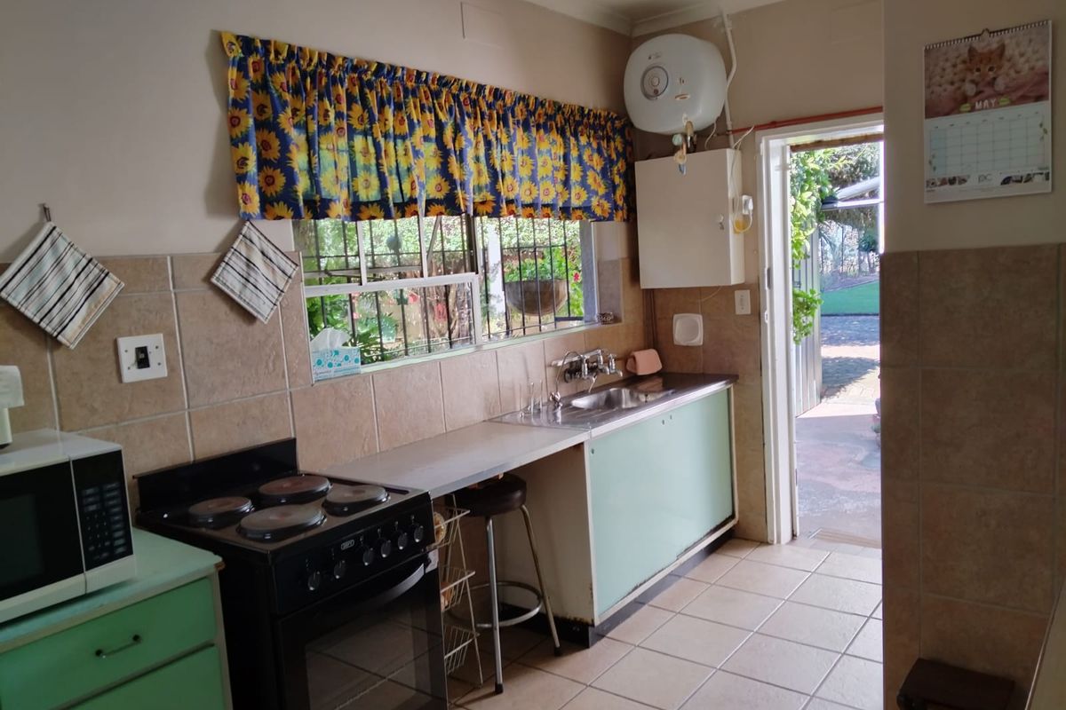 A functional kitchen featuring tiled walls, a freestanding stove, stainless steel sink, and direct access to the rear garden area.