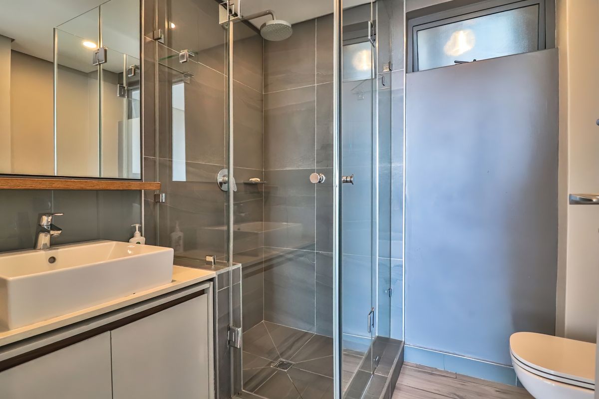 Modern bathroom featuring a glass-enclosed walk-in shower, contemporary vanity with basin, and sleek grey wall tiling.