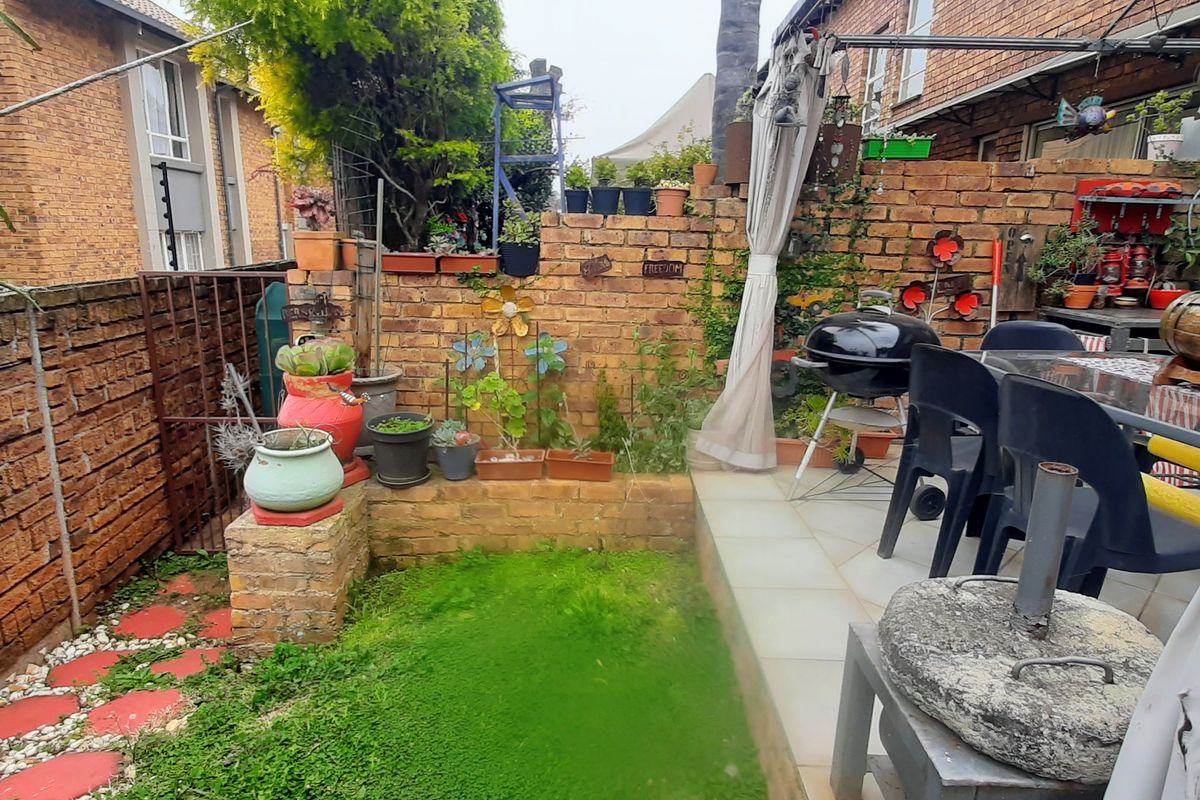 A private rear courtyard featuring a paved patio area, brick boundary walls, and a small lawn section, suitable for outdoor entertaining.