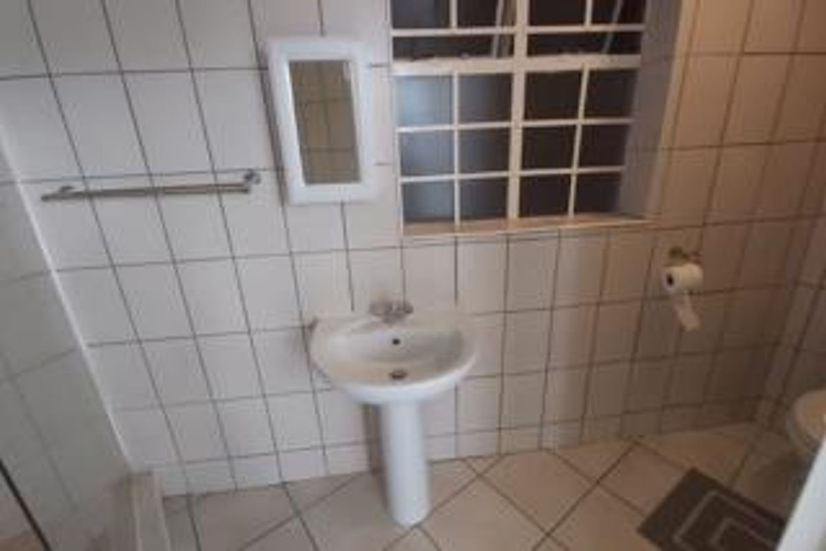A functional bathroom featuring a pedestal basin, tiled walls and flooring, and a window with security bars.