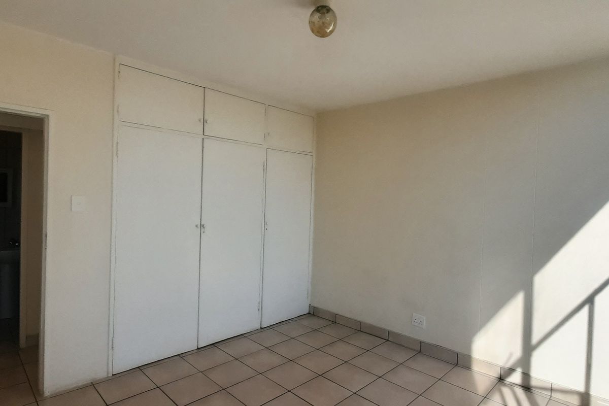A bright, empty bedroom featuring tiled flooring and built-in cupboards, with direct access to an adjacent bathroom.