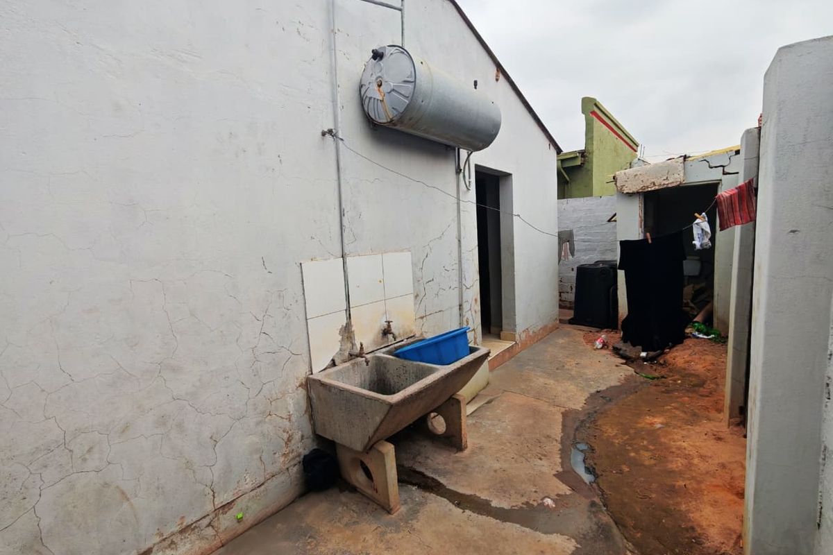 Exterior rear utility area featuring a concrete wash trough, wall-mounted geyser, and paved pathway leading to a secondary structure.