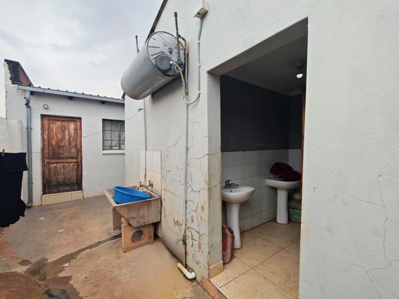Exterior utility area featuring a concrete wash basin, external geyser, and access to a small washroom with two pedestal basins.