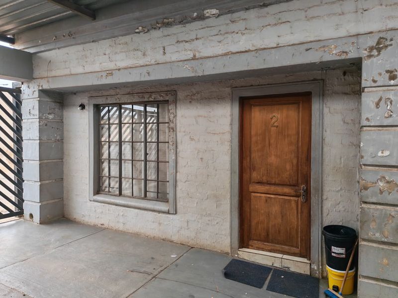 Exterior view of a residential entrance featuring a wooden door, metal-framed window, and covered patio area with weathered brick facade.