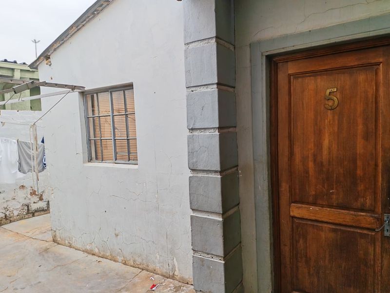 Exterior view of a residential entrance featuring a wooden door and a window with security bars, showing signs of wear on the exterior facade.