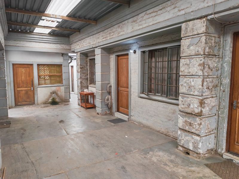 A covered outdoor courtyard area featuring multiple entry doors, concrete flooring, and a corrugated roof structure with translucent panels.