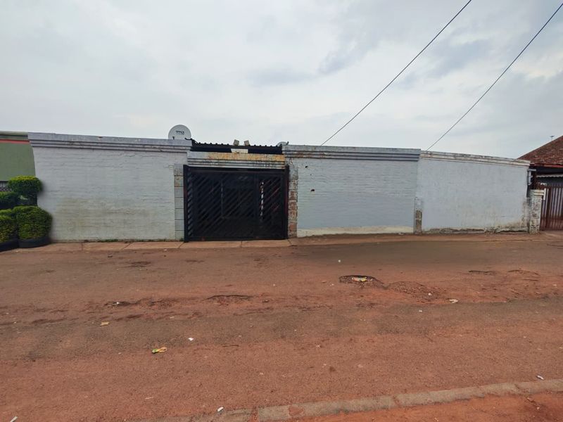 Street view of a property featuring a long perimeter boundary wall and a metal entrance gate.