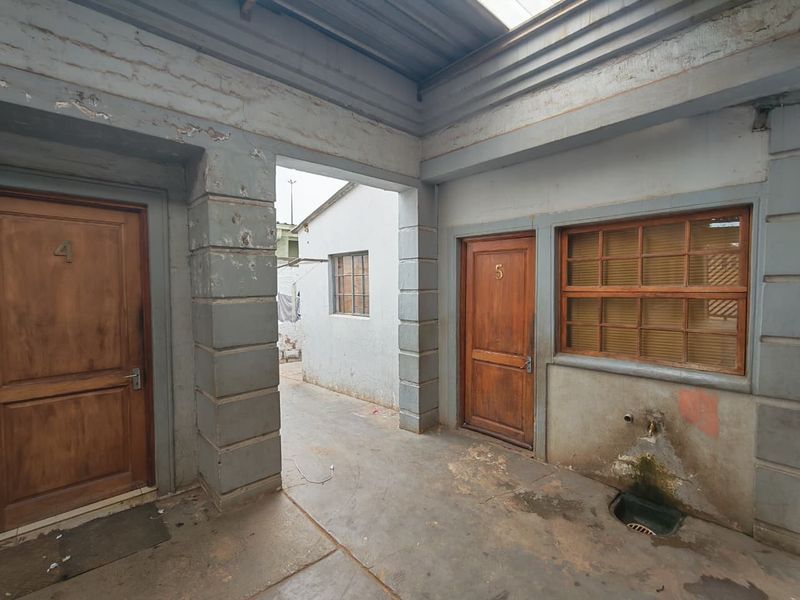 Exterior courtyard area featuring concrete flooring, two wooden entrance doors, and a wall-mounted tap with drainage.