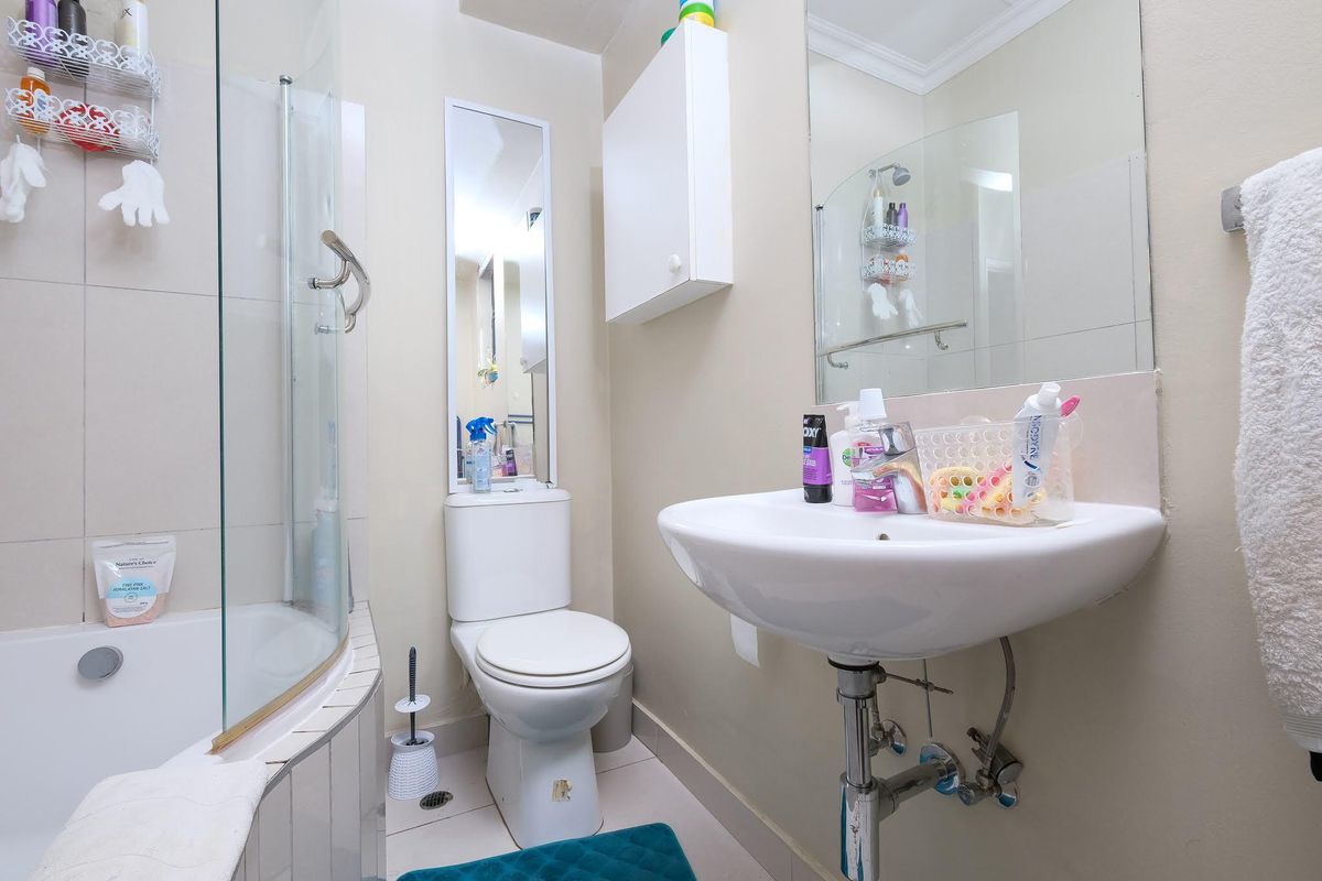 Compact bathroom featuring a wall-mounted basin, a toilet, and a shower-over-bath combination with a glass screen.