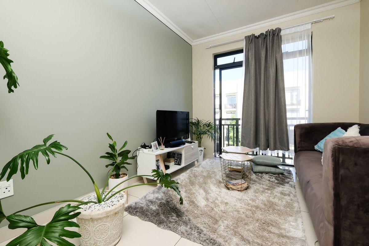 A bright living room featuring tiled flooring, a soft green accent wall, and a sliding glass door providing access to a balcony.