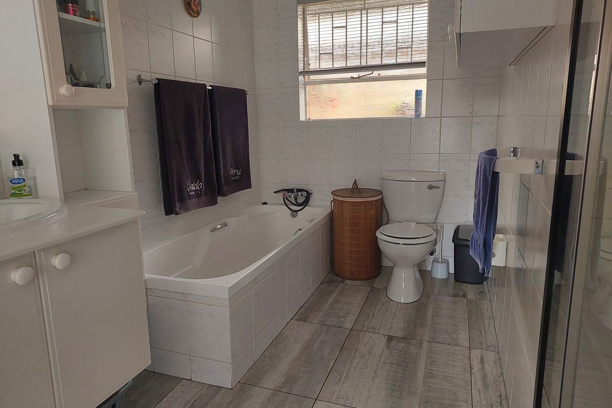 A functional bathroom featuring a built-in bathtub, a standard toilet, and a vanity cabinet with integrated sink, finished with neutral wall and floor tiling.