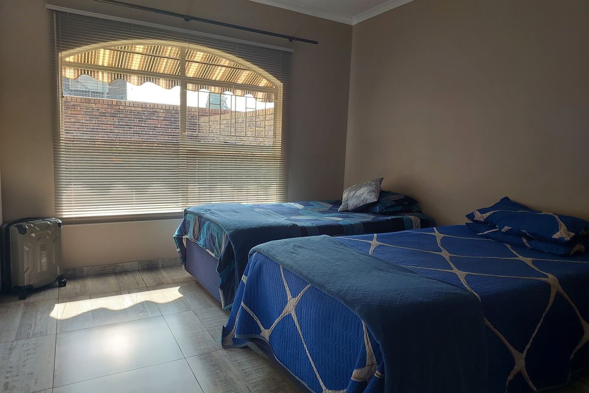 A bedroom featuring tiled flooring and a large arched window with fitted blinds, providing natural light.