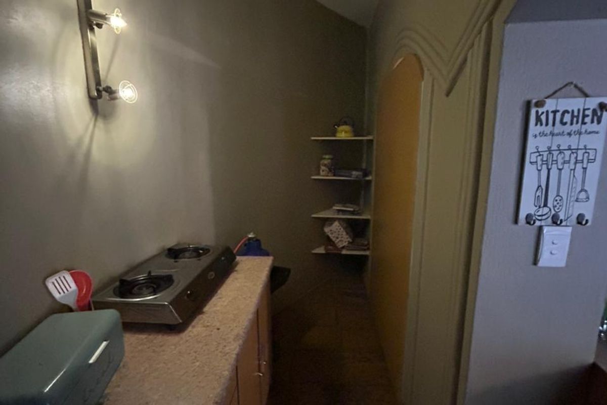 A compact kitchen area featuring built-in cabinetry, a countertop stove, and wall-mounted shelving in a narrow layout.