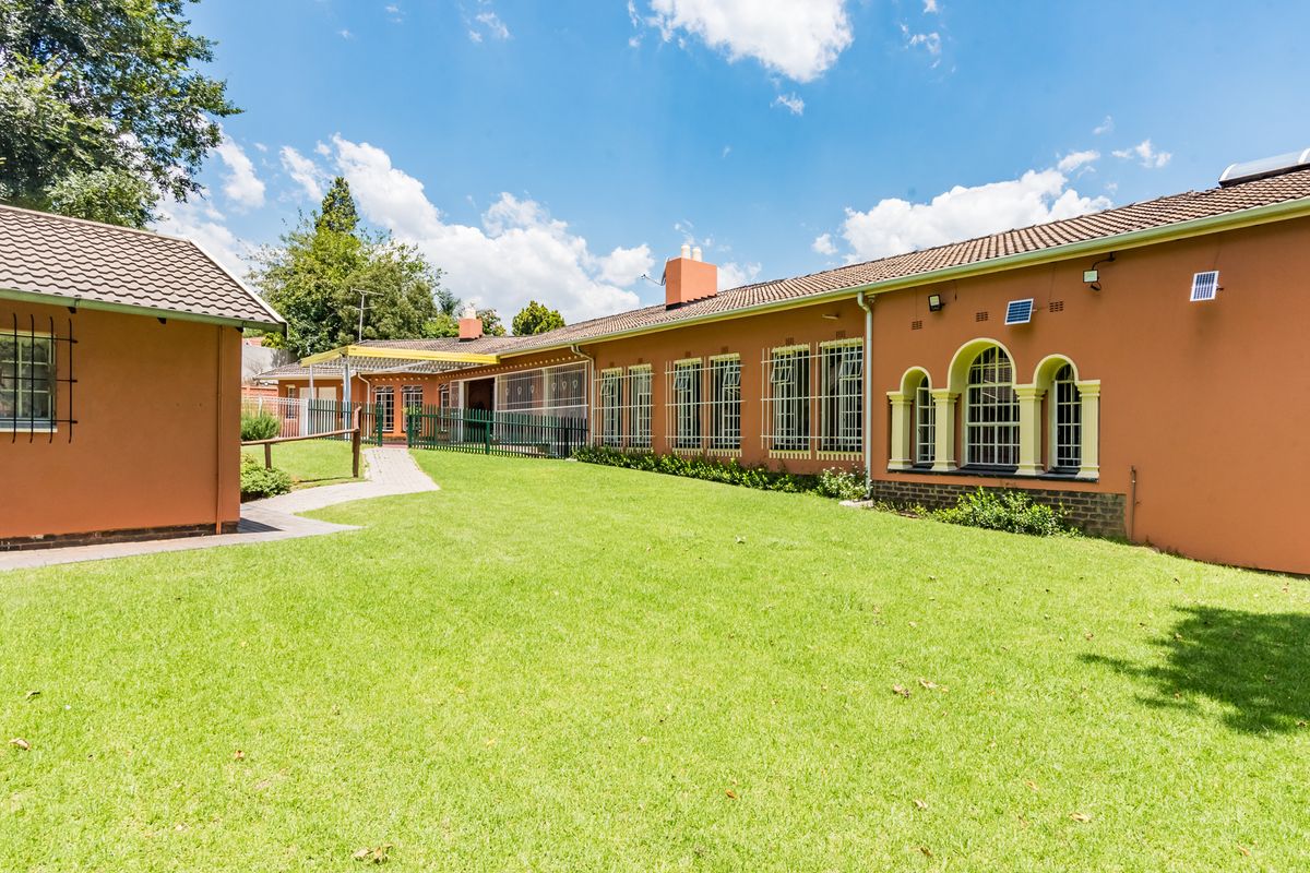 A spacious rear garden area featuring a well-maintained lawn, paved walkway, and the rear elevation of the house with arched window detailing.