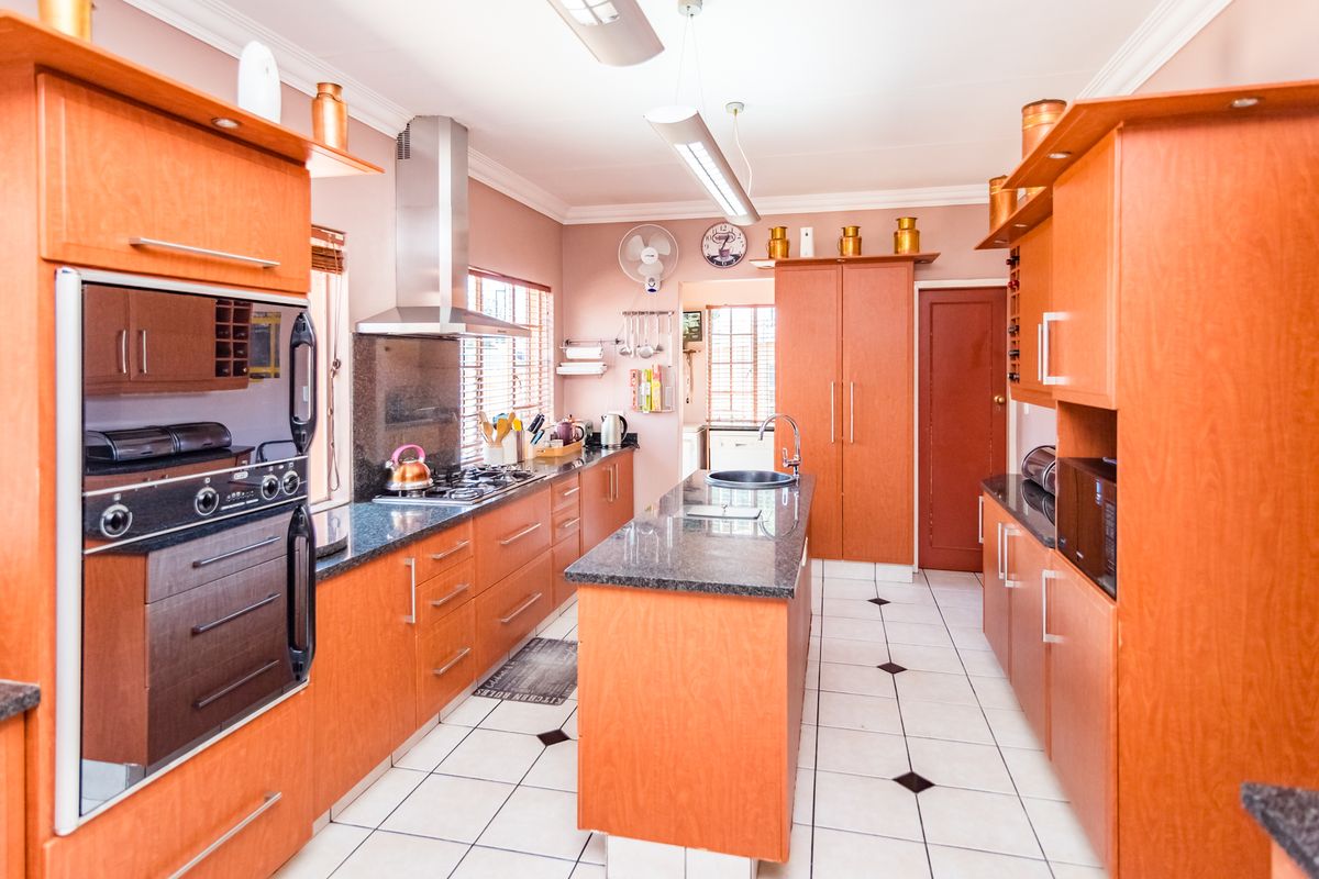 A functional kitchen featuring wooden cabinetry, granite countertops, a central island with a sink, and built-in stainless steel oven and extractor fan.