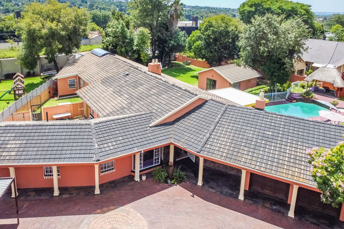 Aerial view of the property featuring a tiled roof, paved driveway, swimming pool, and landscaped garden area.