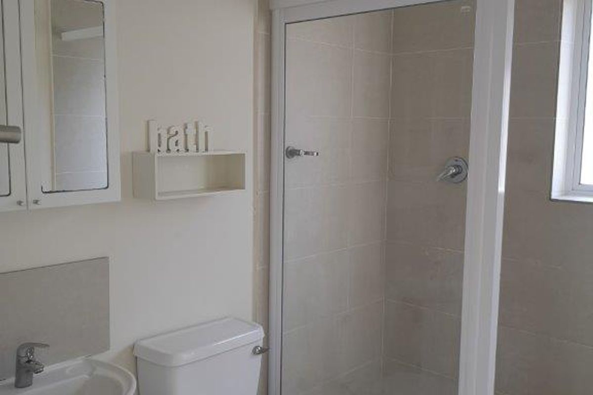 A functional bathroom featuring a pedestal basin, a white toilet, and a tiled shower enclosure with a glass door.