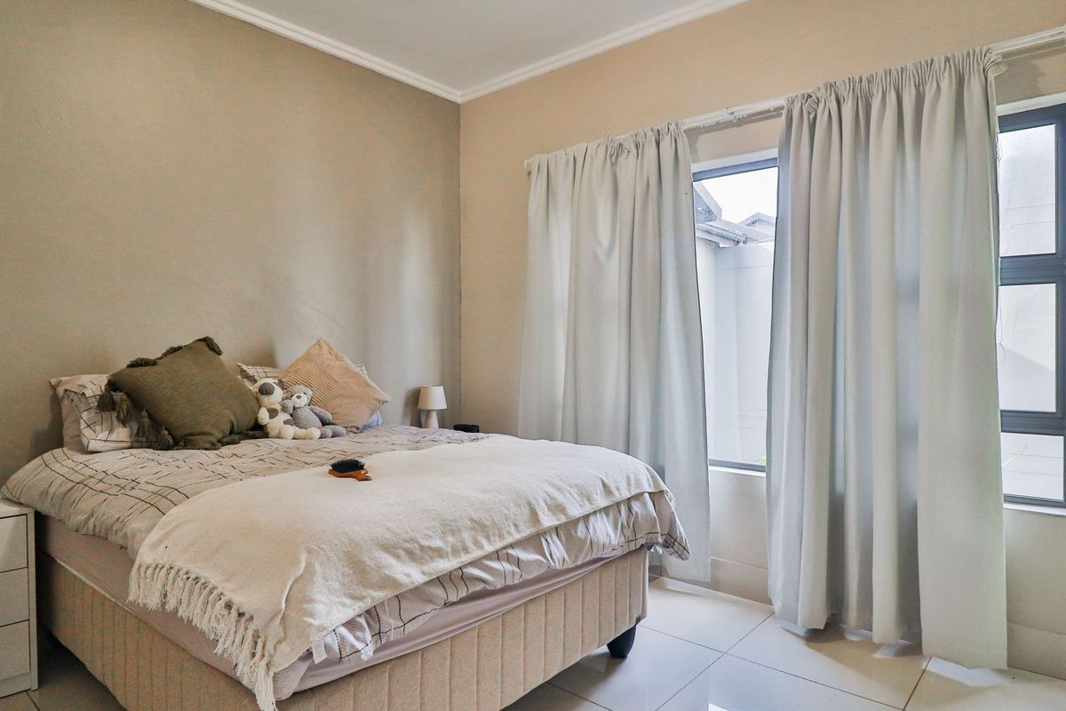 A well-maintained bedroom featuring neutral wall tones, tiled flooring, and a large window with curtain tracks, providing natural light and a clean aesthetic.
