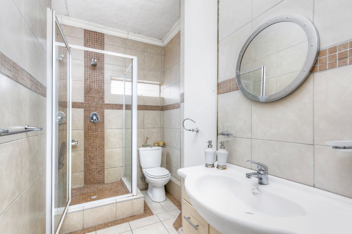A functional bathroom featuring a glass-enclosed shower, a pedestal vanity with a basin, and neutral wall tiling with decorative mosaic accents.