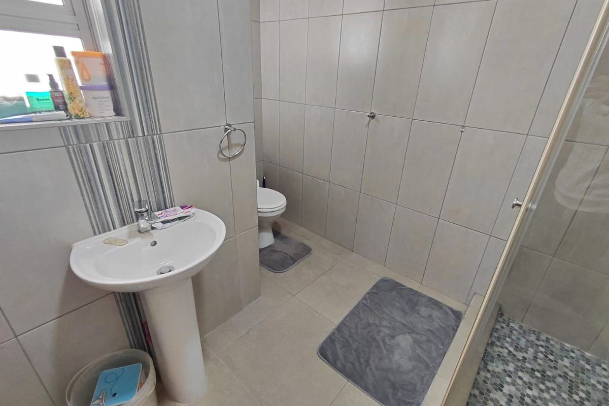 A functional bathroom featuring a pedestal basin, toilet, and a glass-enclosed shower with neutral wall and floor tiling.