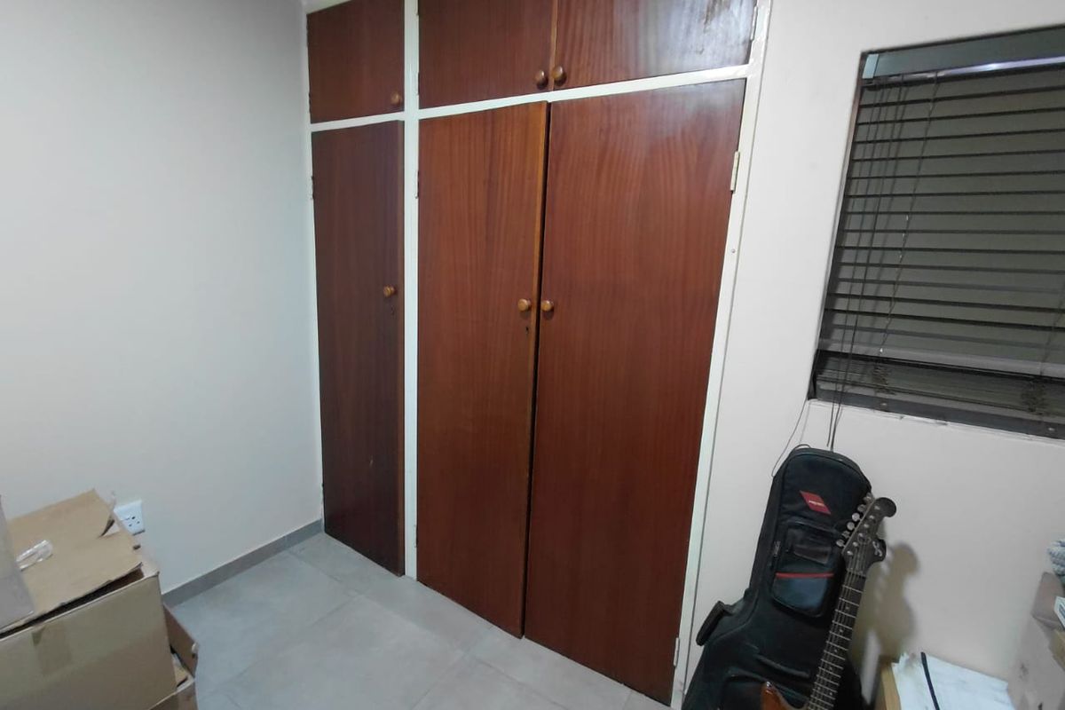 A bedroom featuring floor-to-ceiling built-in wooden cupboards and a window fitted with venetian blinds.