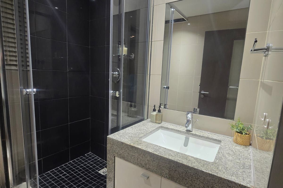 Modern bathroom featuring a glass-enclosed shower with dark tiling, a granite vanity top with an integrated basin, and a large wall-mounted mirror.