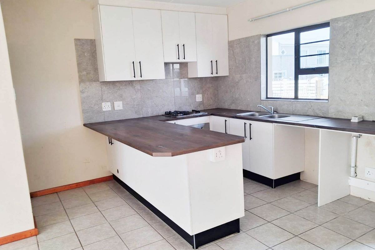 A clean, functional kitchen featuring white cabinetry, dark laminate countertops, a gas hob, and neutral tiled flooring, offering a bright and practical workspace.