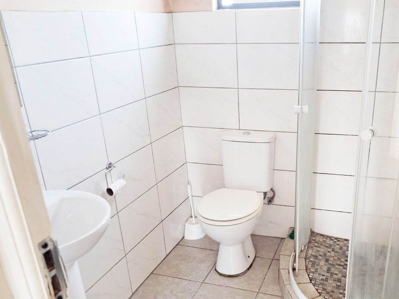 A functional bathroom featuring a pedestal basin, toilet, and a corner shower enclosure with tiled walls and flooring.