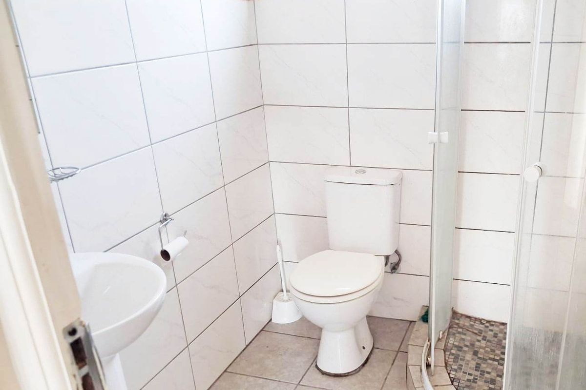A functional bathroom featuring a pedestal basin, toilet, and a corner shower enclosure with tiled walls and flooring.