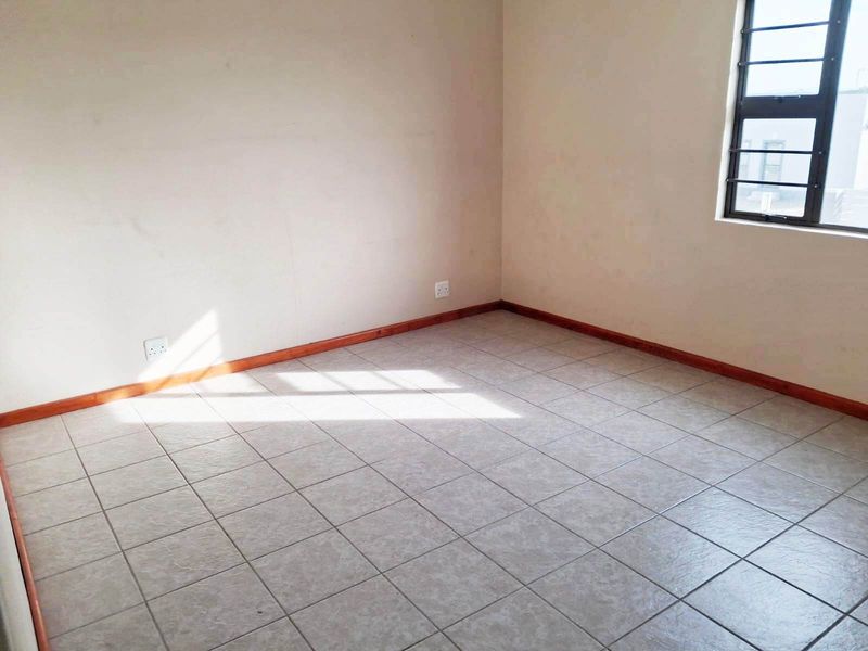 An empty bedroom featuring neutral tiled flooring, timber skirting boards, and a window fitted with security bars.